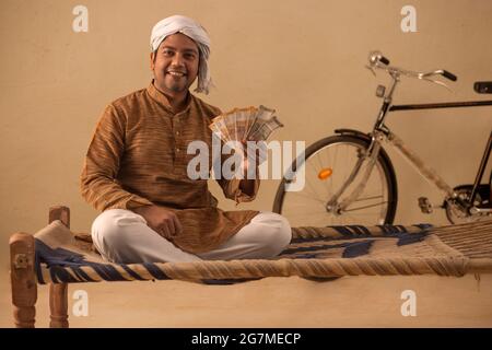 A TURBANED RURAL MAN HAPPILY HOLDING MONEY AND POSING IN FRONT OF CAMERA Stock Photo