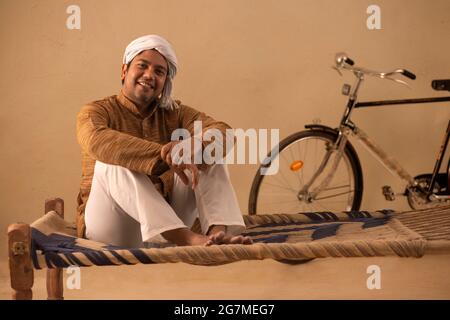 A RURAL MAN COMFORTABLY SITTING ON COT AND LOOKING AT CAMERA Stock Photo