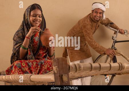 A TURBANED RURAL MAN LOOKING AT WIFE WHILE SHE PUTS MONEY IN PIGGY BANK Stock Photo