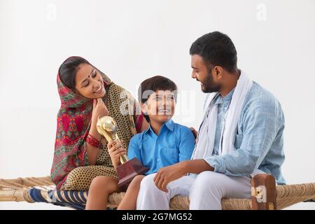 PORTRAIT OF A RURAL BOY SHOWING HAPPILY HIS TROPHY TO PARENTS Stock Photo