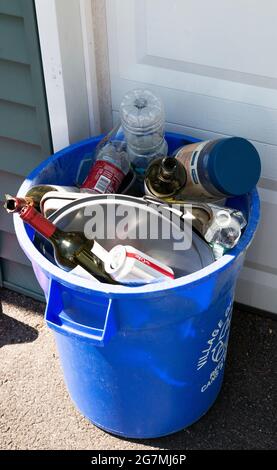 Babylon, New York, USA - 15 May 2021: Overhead view of a blue wrap recycling can full of bottles and cans in front of a residential garage. Stock Photo