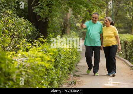 A SENIOR ADULT HUSBAND POINTING TOWARDS GARDEN WHILE WALKING WITH WIFE Stock Photo