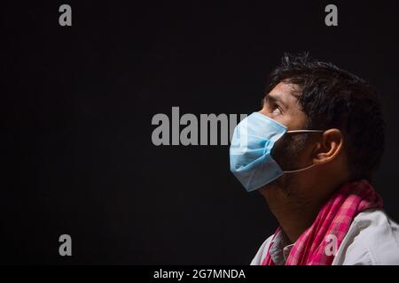 A LABOURER WEARING FACE MASK SITTING ALONE AND LOOKING ABOVE Stock Photo