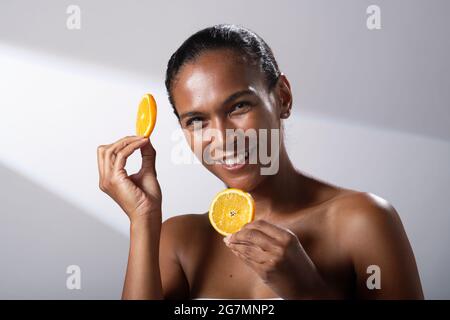 Beauty images of a woman with darker skin tone. Head and shoulder pictures of smiling, happy lady. Holding a slice of orange fruit. Stock Photo