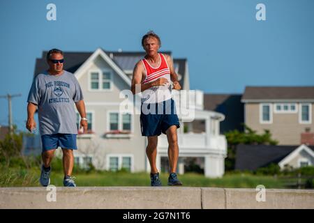 North Wildwood, United States. 15th July, 2021. People run and walk on the concrete bulkhead along the Atlantic Ocean on a warm summer day Thursday, July 15, 2021 at in North Wildwood, New Jersey. Temperatures are expected in the 90's through the rest of this week. Credit: William Thomas Cain/Alamy Live News Stock Photo