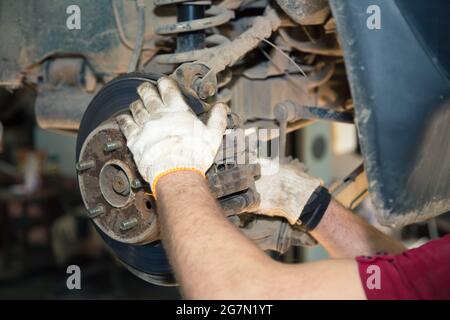 The gloved hands of a man unscrew the caliper on the hub. In the garage, a man changes parts on a vehicle. Small business concept, car repair and maintenance service. UHD 4K. Stock Photo