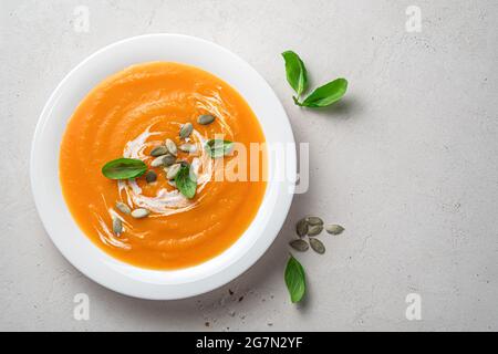 Pumpkin soup puree with cream and basil in a white plate on a gray background. Stock Photo