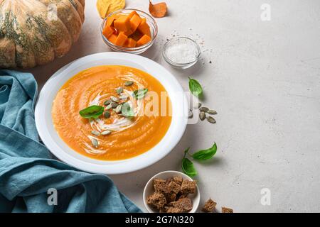 Autumn pumpkin soup in a white plate on a gray background with pumpkin, spices and rye crackers. Stock Photo
