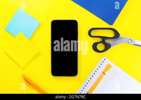 Back to school. Education flat lay. Business layout. Mobile phone mock up, notepad, pen, sticker paper, scissors on yellow background. Copy space Stock Photo