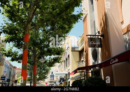 Las Rozas outlets shopping mall with a Clarks shoes store and orange banding on trees to repel insects on a sunny summer afternoon Madrid Spain Stock Photo