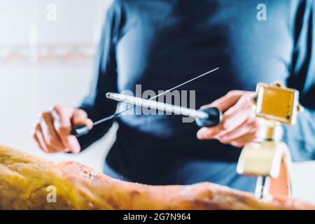 Anonymous person sharpening ham knife before cutting ham. Very well sharpened quality knife. Midsection of male chef's sharp knife in the kitchen. Stock Photo
