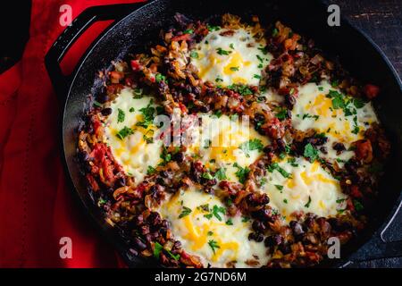 Mexican Baked Eggs in a Cast Iron Skillet: Baked eggs, black beans, and tomatoes served in a cast iron pan Stock Photo