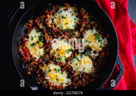 Mexican Baked Eggs in a Cast Iron Skillet: Baked eggs, black beans, and tomatoes served in a cast iron pan Stock Photo