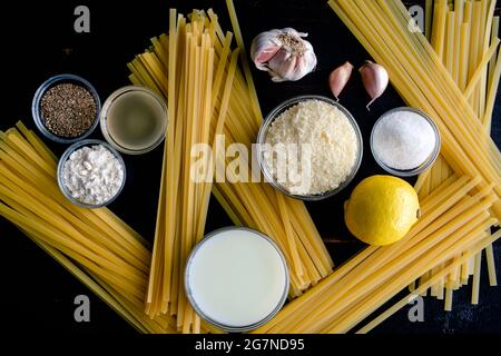 Fettuccine Alfredo Ingredients on a Wood Background: Raw pasta, garlic, parmesan cheese, and other ingredients on a dark wooden table Stock Photo