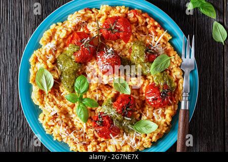 creamy tomato risotto with cherry tomatoes and sauce pesto on a blue plate, flat lay, macro Stock Photo