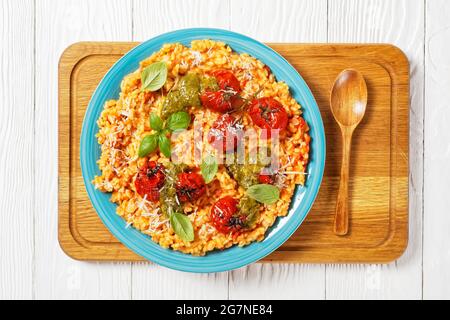 creamy tomato risotto with cherry tomatoes and sauce pesto on a blue plate on a cutting board Stock Photo