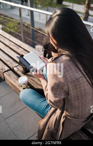 Long-haired brunette woman reading an electronic book with blank screen. View from behind Stock Photo