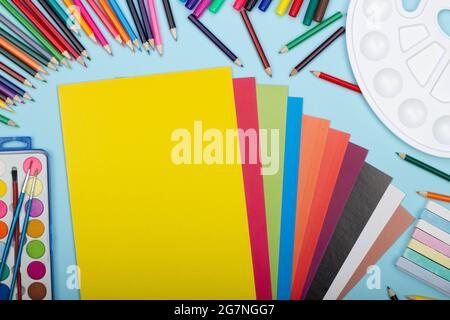 Art school supplies for painting and a set of colored paper on a blue background with copy space for text. Colorful pencils, markers, paints, crayons. Stock Photo