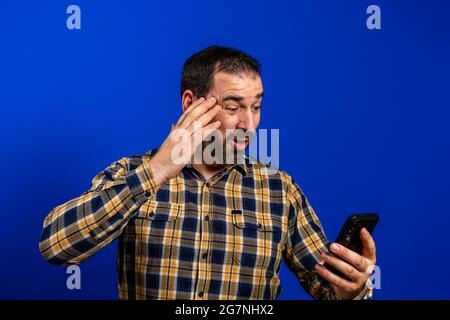 Full length portrait of a cheerful handsome young man standing isolated over blue background, holding mobile phone. Stock Photo