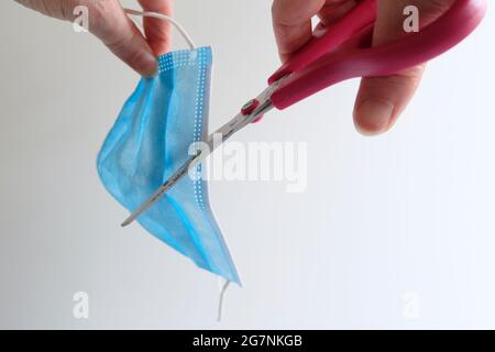 Hands of a mature adult taking a pair of scissors to a blue face mask