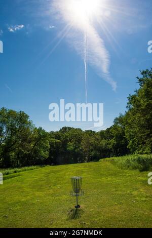 Sunlight and a jet contrail seem to point to and highlight a summertime disc golf goal. Stock Photo