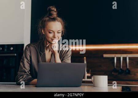 Young girl worker in pajamas drinks morning coffee in kitchen Stock Photo