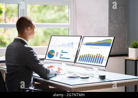 Businessman In Office At Desk Using Graphs On Computer Monitor Stock Photo