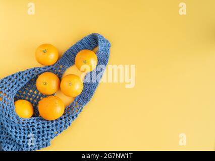 Hand-woven blue bag with oranges on yellow background. Copy space. Top view. Stock Photo