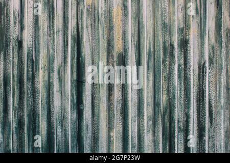 Texture of rusty metal surface with vertical stripes or slats and cracked paint in tones of green, white and yellow. Old weathered gate background Stock Photo