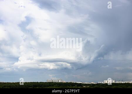 gray rainy clouds with whirls over city and forest on June day Stock Photo