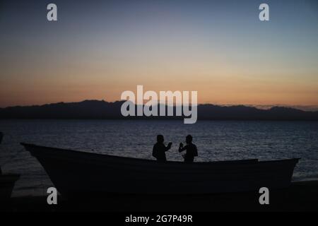 HERMOSILLO, MEXICO - JUNE 28: Two people toast at sunset next to a fishing boat and the silhouette in the background of Isla del Tiburon, during a show as part of festival to defend water and preserve the indigenous Seri's customs on June 28, 2021 in Hermosillo, Mexico. (Photo by Luis Gutierrez/Norte Photo) Stock Photo