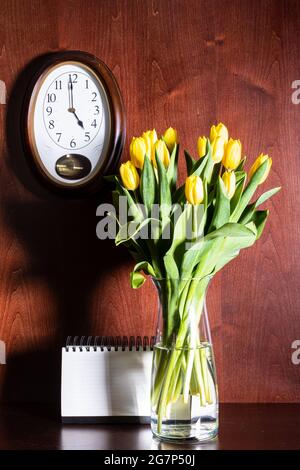 wall clock, blank calendar and tulips in vase on dark brown wooden background Stock Photo