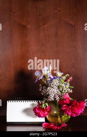 withered flowers in vase and blank calendar on dark brown wooden background Stock Photo