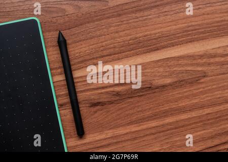 Top view of a graphics tablet with a pen on a wooden table Stock Photo