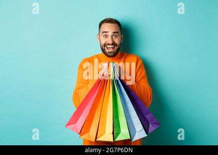 Excited adult man holding shopping bags and smiling, going to mall, standing over turquoise background Stock Photo