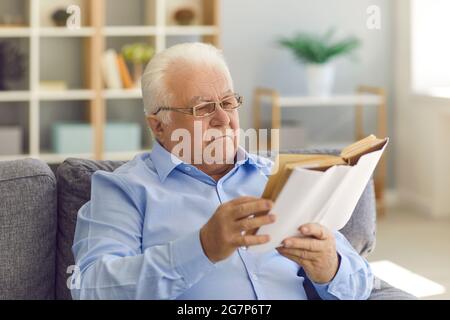 Serious senior man in new eyeglasses sitting on the couch and enjoying a good book Stock Photo