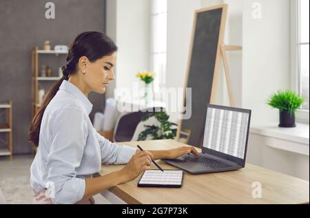 Woman sitting at office desk, working on laptop and tablet computers and using stylus pen Stock Photo