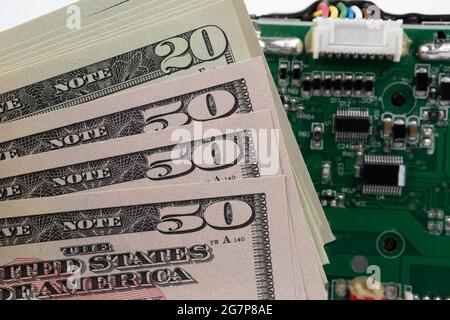 Stack of American dollar banknotes and blurred Printed circuit board on the background. Concept. Stock Photo