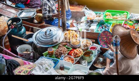 Woman wearing a straw hat in a boat, selling vegetables and fruits at a floating market in Thailand, connected to a 2nd boat. Stock Photo