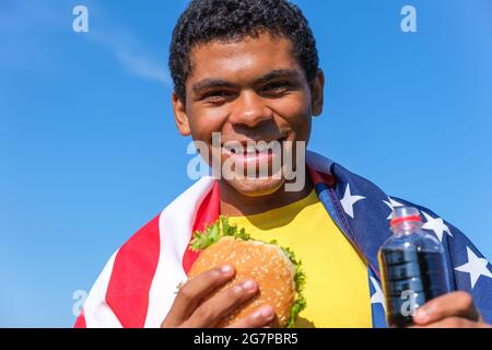 African American man with flag enjoying hamburger and cola drink outdoor Stock Photo