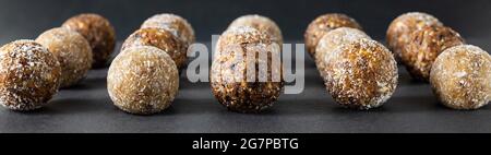 Homemade energy balls on a dark background closeup. Banner. Candy with dried apricots, raisins, dates, prunes, walnuts, almonds and coconut. Stock Photo