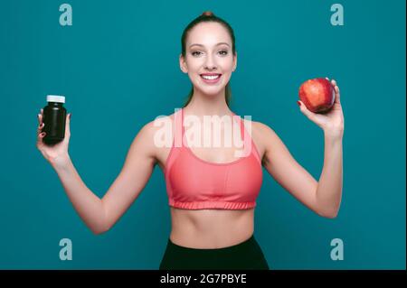 Young smiling sporty female shows apple and pills or drugs on green isolated background Stock Photo