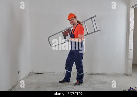 in a dark overalls, a cheerful engineer holds a stepladder Stock Photo