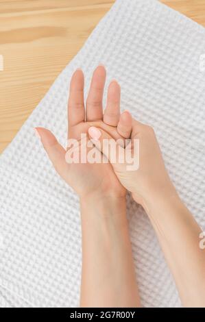one female hand massages the other hand lying on a white towel with the open palm up. vertical image. Closeup hand of person massage her hand from pai Stock Photo