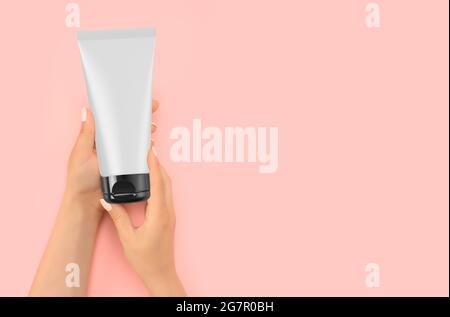 Hand holding mockup Cosmetic plastic tube isolated on pink background. Cream Tube in Hand Cream On Soft Silky Healthy Skin Care Concept . Beautiful Wo Stock Photo