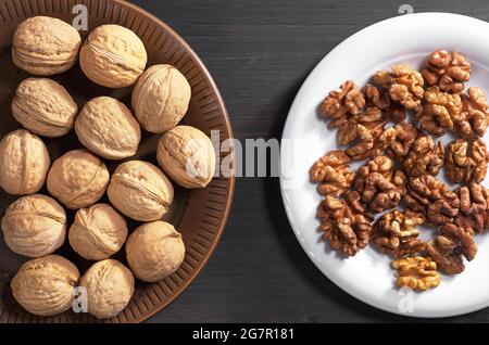 Walnuts whole and kernels in plate on dark wooden table, top view Stock Photo