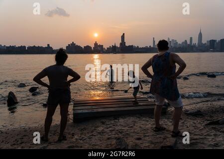 New York, USA. 07th July, 2021. People enjoy the sunset on the banks of the East Rvier in Brooklyn with the Manhattan skyline in the background. New York is well on its way to making up for its enforced Corona timeout with a historic 2021. The 'Summer of Freedom' has long been compared to that of love in 1967. (to dpa: 'New York's golden summer - and the growing shadow') Credit: Mathias Wasik//dpa/Alamy Live News Stock Photo