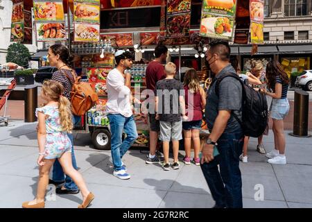 New York, USA. 11th July, 2021. Passersby walk by a hot dog stand on 5th Avenue. New York is well on its way to making up for its enforced Corona timeout with a historic 2021. The 'Freedom Summer' has long been compared to the 1967 Love Summer. (to dpa: 'New York's golden summer - and the growing shadow') Credit: Mathias Wasik//dpa/Alamy Live News Stock Photo