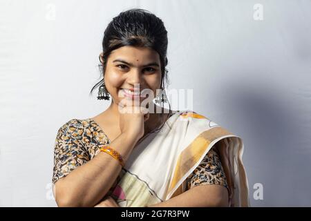 Isolated on white background an Indian female in saree smiles to camera with hand under chin pose on white background Stock Photo