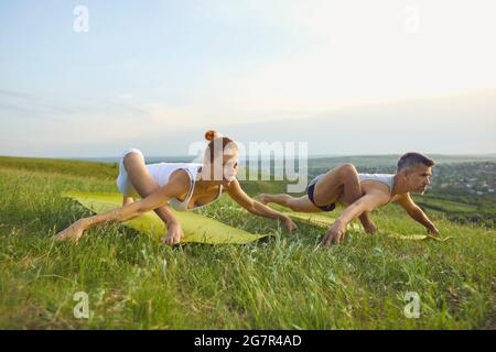 Man and woman doing forward bending yoga exercises on green grass of summer meadow Stock Photo